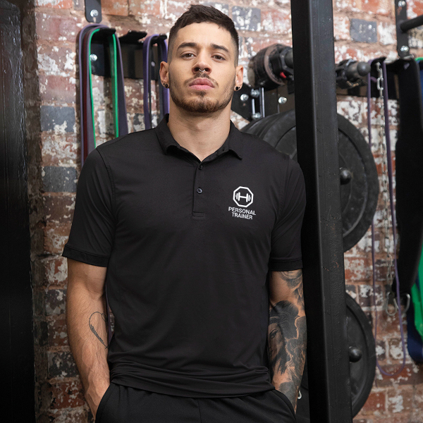Male fitness professional wearing a black polo shirts personalised with logo standing in gymnasium